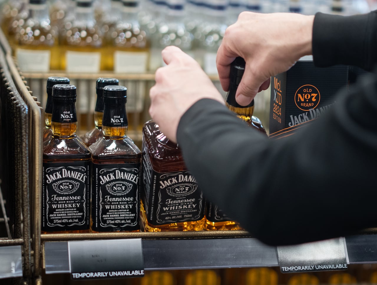 A person's hands lift bottles of whisky off a shelf.