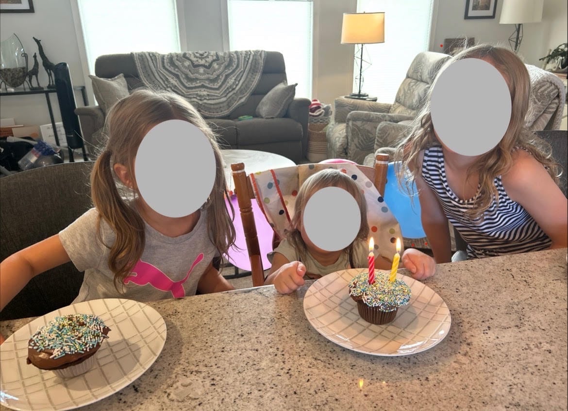 Three children with their faces blurred sit in front of cupcakes