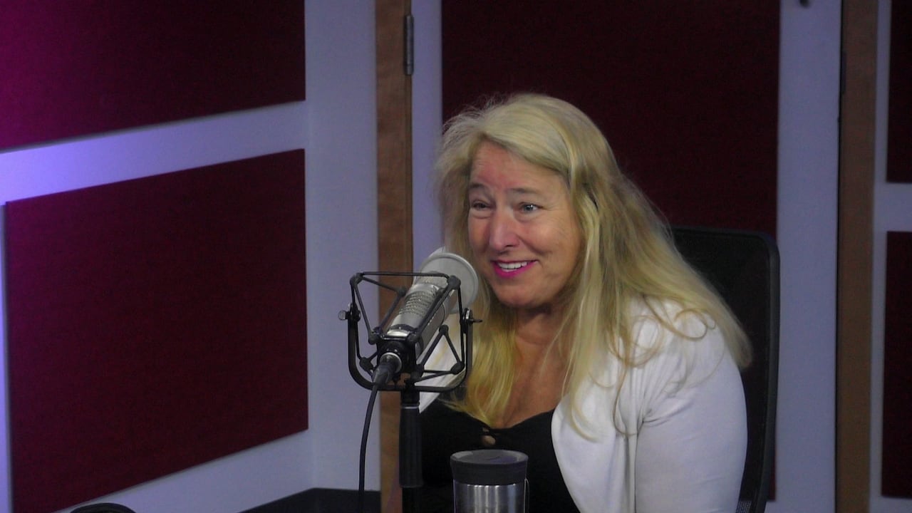 Woman in white cardigan speaks into microphone.