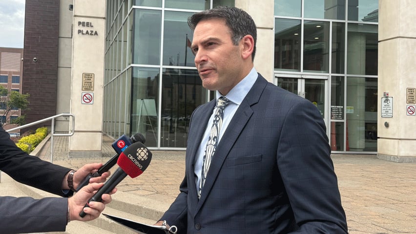 A man in a suit speaking into reporters' microphones.