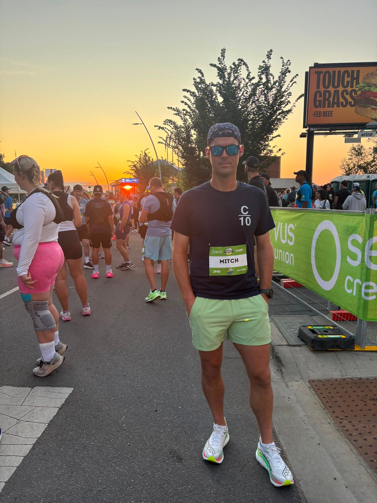 A man in green shorts and a black shirt with sunglasses stands on a sunny morning.