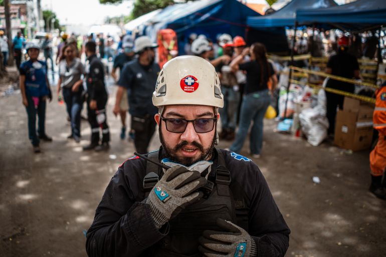 Enrique Zapata, head of logistics at NGO SARES, coordinates other aid workers via walkie-talkie at the site of the collapsed Vanessa apartment building. [Euan Wallace / Al Jazeera]