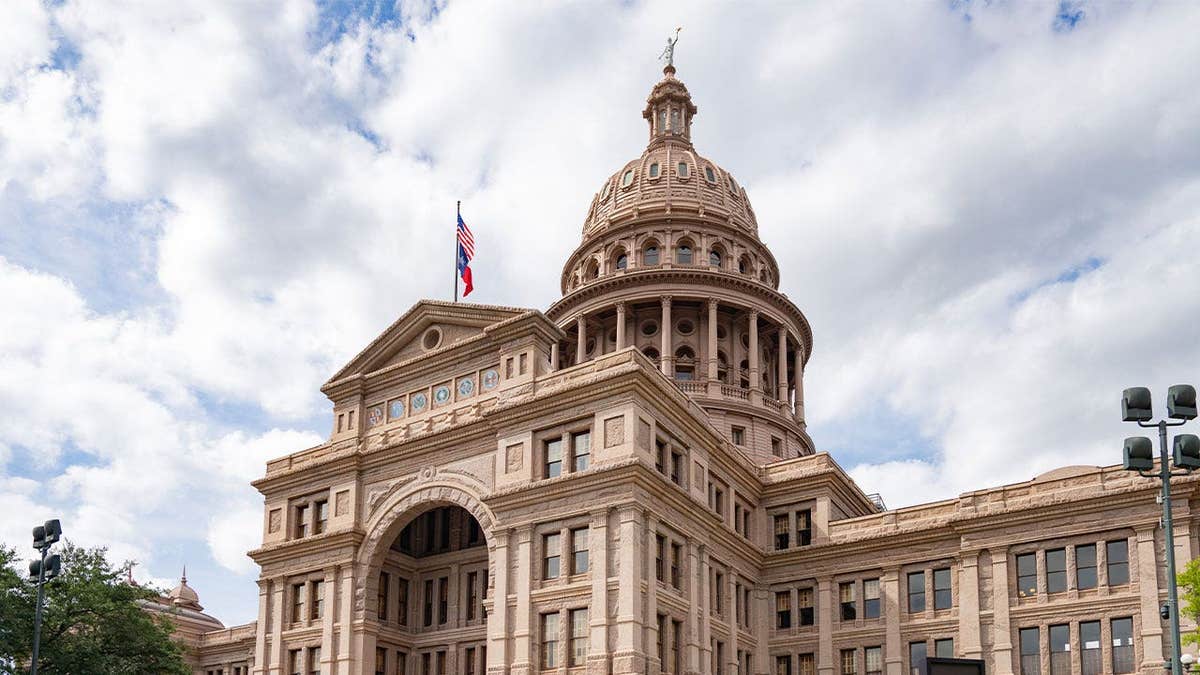 Texas State Capitol building in Austin under a partly cloudy sky, with U.S. and Texas flags flying above the entrance