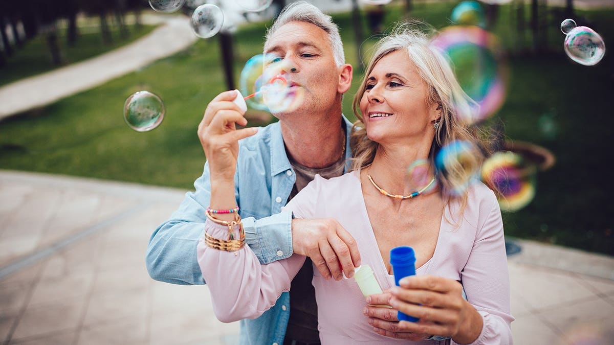 Senior couple blowing bubbles together at the park.