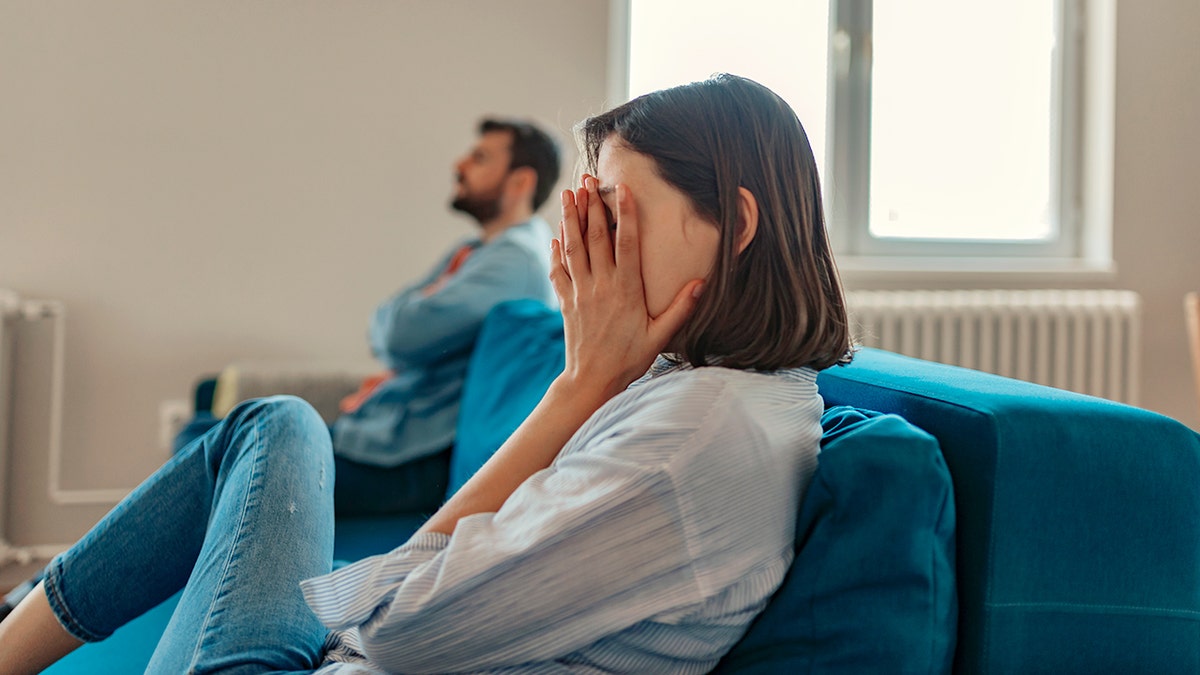 unhappy couple sit on couch while woman hides her face