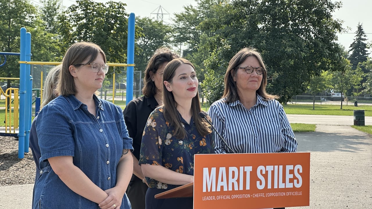Five women stand before a lectern on a playground. The lectern has a sign reading "Marit Stiles."