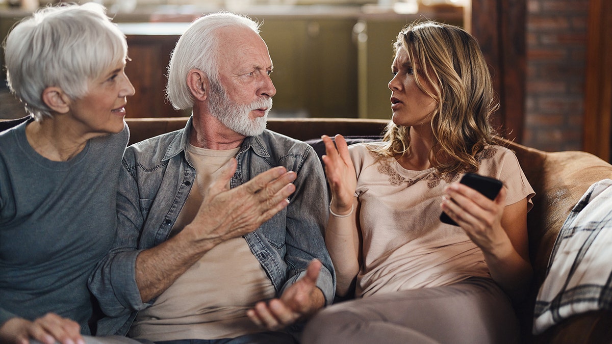 Elderly senior couple arguing with young woman on couch.