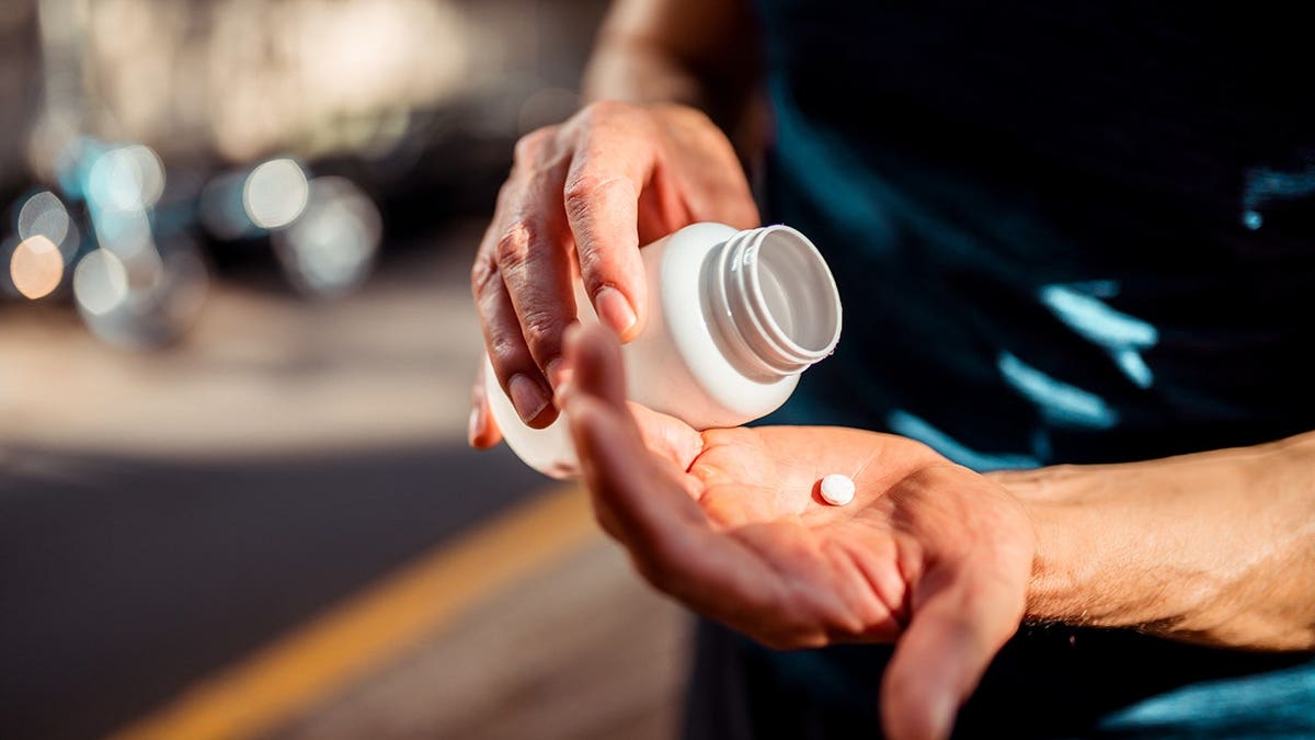 Hands hold a medicine bottle and a pill.