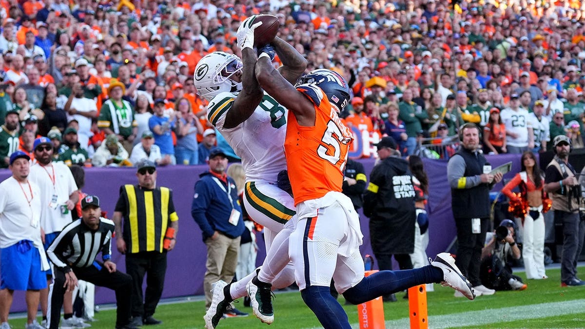 Josh Jacobs catches a touchdown pass under pressure from Dre Greenlaw during an NFL game.