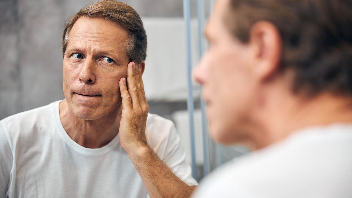 Middle-aged man stares at his reflection in a mirror.