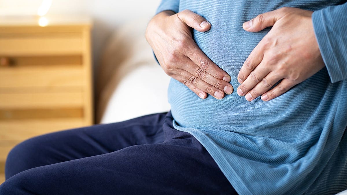 Man sitting on his bed, holding his stomach.