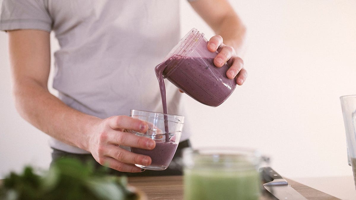 Young man pours blended smoothie into a glass.