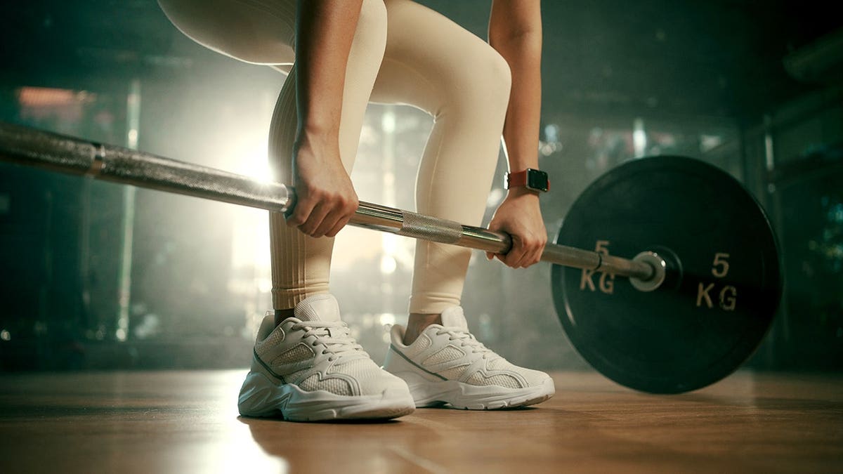 Young woman deadlifts a heavy barbell in a gym.