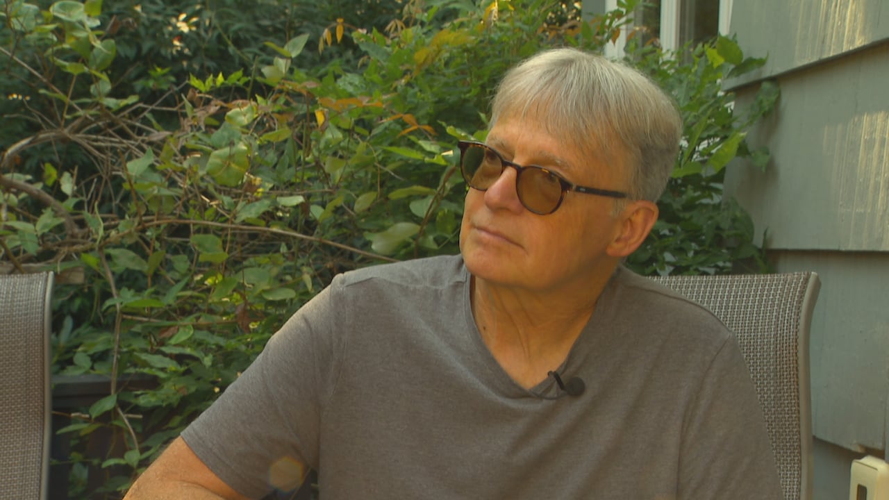 A silver-haired man sits in a chair in his backyard.