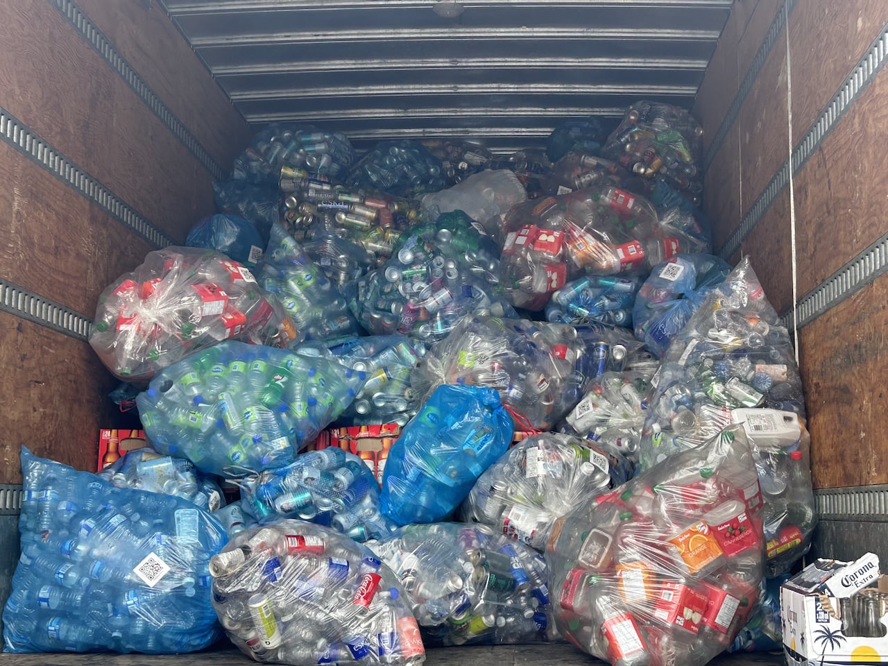 bags full of empty bottles and cans sit in the back of a truck.