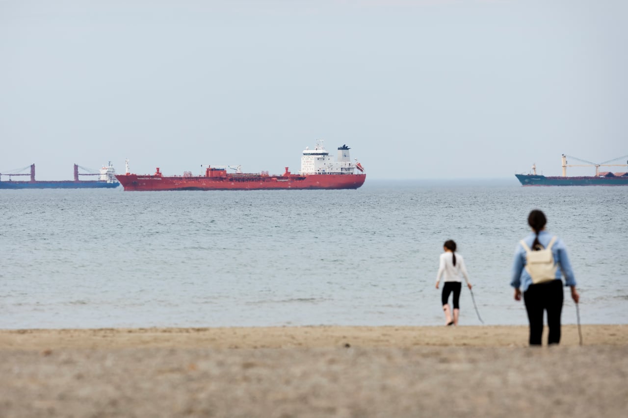 Two people on a beach near a body of water with three large ships on it.