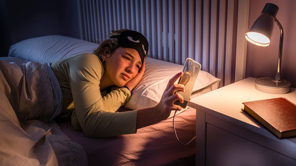 Teenage girl checking time on smartphone in bed at night