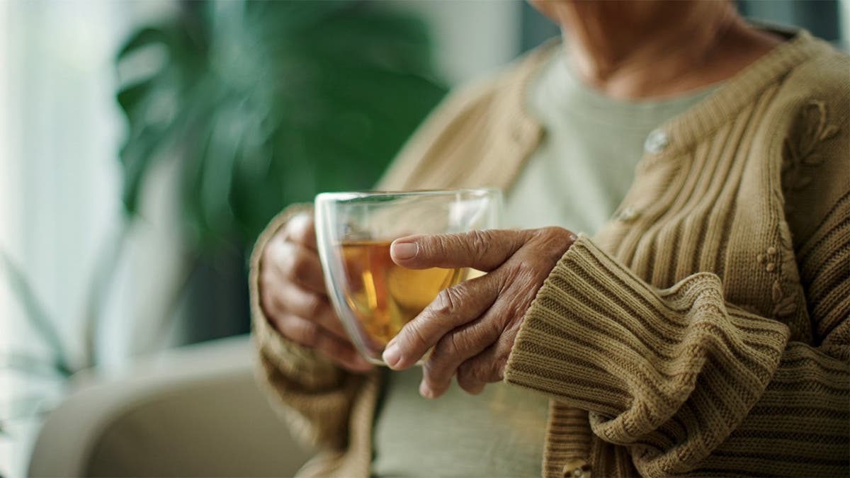 An older woman sits and holds a cup of tea.