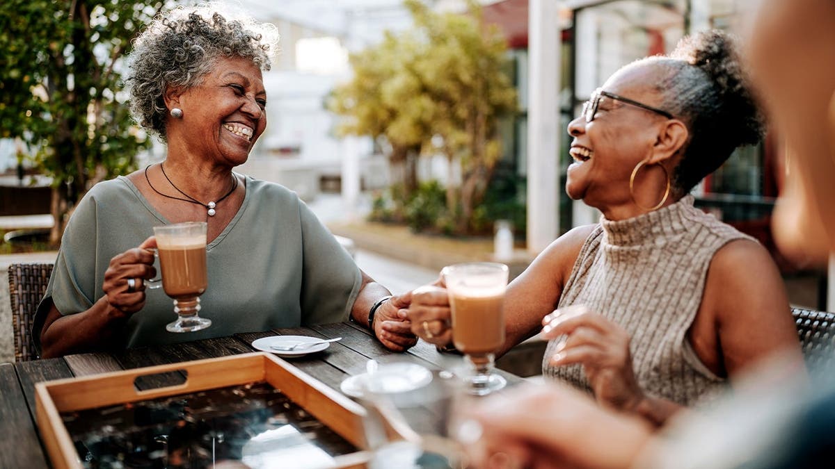 Two women laugh and enjoys cups of coffee together.